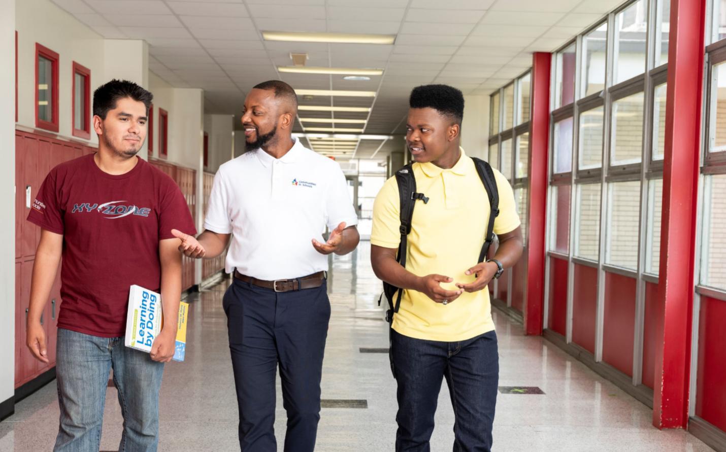 Two students and an adult walk the halls of a high school.